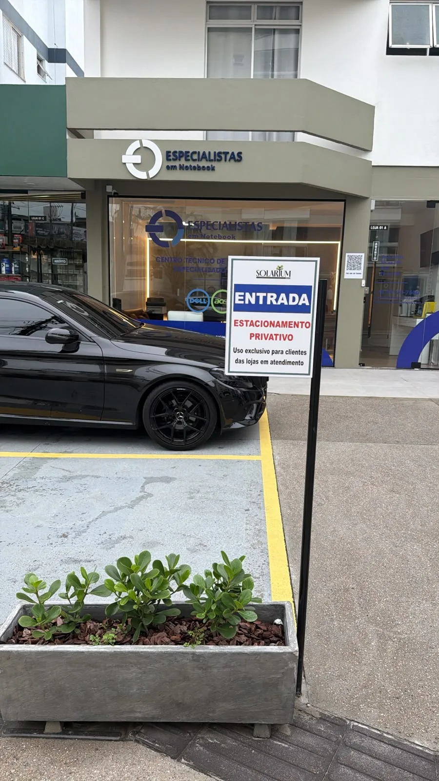 Placa de entrada do estacionamento privativo com carro estacionado em frente à loja
